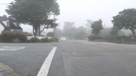 Typical generic suburban residential district street, detached houses homes, foggy misty road, Monterey California USA. Neighborhood suburb. Rainy weather, moody atmosphere, silent city in haze brumeの写真素材