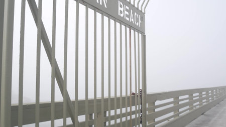 Metal gate on Ocean Beach pier in fog, misty California coast, USA. Foggy moody cloudy weather on San Diego shore. Calm tranquil atmosphere. Waterfront boardwalk entrance in gloomy depressive haze.の写真素材
