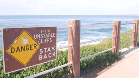 Ocean waves crashing on beach or bluff, La Jolla shore waterfront promenade, California USA. Succulent green ice plant, pacific coast. Seascape view and railings. Danger unstable cliff warning sign.の写真素材