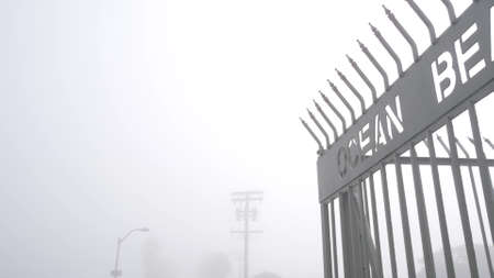 Metal gate on Ocean Beach pier in fog, misty California coast, USA. Foggy moody cloudy weather on San Diego shore. Calm tranquil atmosphere. Waterfront boardwalk entrance in gloomy depressive haze.の写真素材