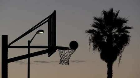 Hoop, net and backboard for basketball game silhouette, sunset sky. Basket ball court on street,...