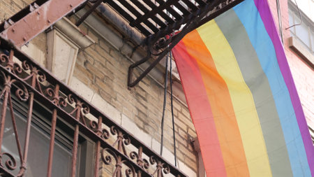 New York City building architecture, Manhattan USA. Urban residential house exterior. LGBT rainbow flag, United States. Typical red brick facade. Fire escape emergency ladder. Homosexual symbol. Prideの写真素材