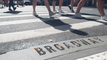 Broadway street sign, people on pedestrian zebra crossroad. New York City Manhattan road intersection. Text on asphalt near crosswalk, shadows on crossroad ped crossing. Traffic signage, United Statesの写真素材