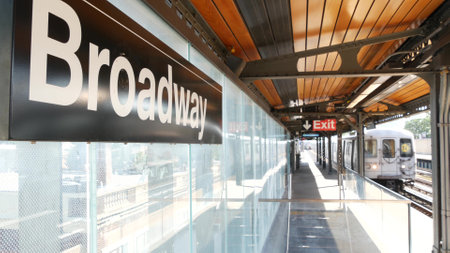 New York subway station Broadway text sign. Metropolitan train on platform, United States public metro transportation. Elevated outdoor railway line, Astoria, Queens. NYC passenger railroad traffic.の写真素材
