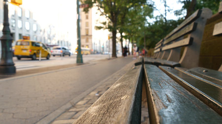 Wooden bench near Central Park in New York City, United States. Cars and people on street in...