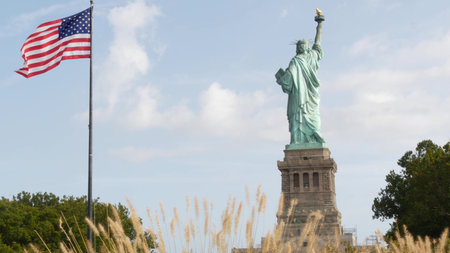 Statue of Liberty on Liberty Island, New York, United States. Democracy and patriotism symbol near Manhattan, NYC USA. American flag waving in wind. Independence concept.の写真素材