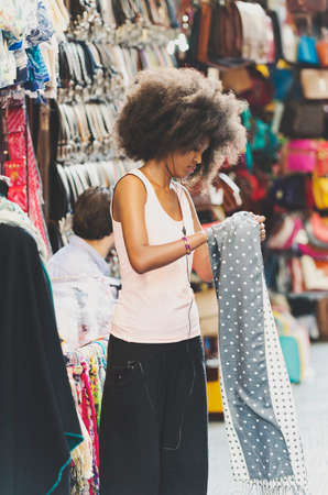 Florence, Italy - June 28, 2014: Beautiful black girl with magnificent hair does the job in a clothing stall in the local market in the heart of Florence. The beautiful girl puts in order the clothes while listening to music with headphones in the ears onのeditorial素材