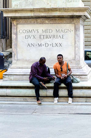 Florence, Italy - June 28, 2014: two african black man sitting at the base of the column of the Trinity Square in the heart of Florence in Italyのeditorial素材