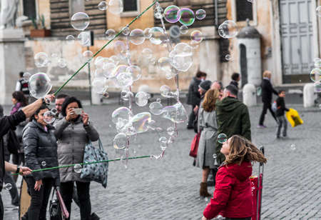 Rome, November 2017 Italy: An artist is making big soap bubbles for kids with special device. Kids are running and trying to catch them. Photo shoot at Piazza Popolo in Rome, Italy,のeditorial素材