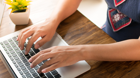 Woman hands typing on laptop keyboard on wooden table at homeの写真素材