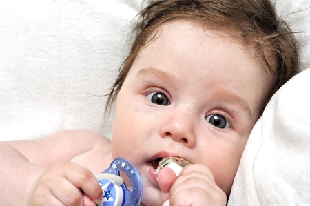Baby in bed with dummy and silver toyの写真素材