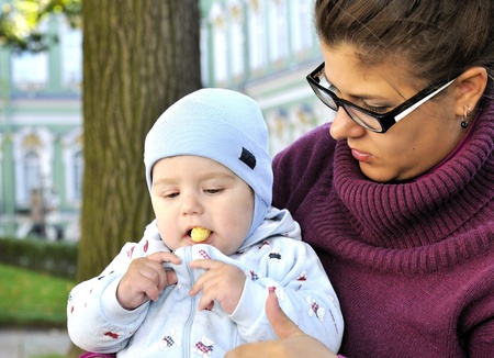 Baby sits on mother lap and eats corn ball