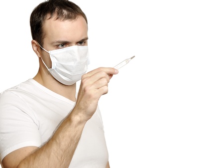 Sick young man in medical mask looks at thermometerの写真素材