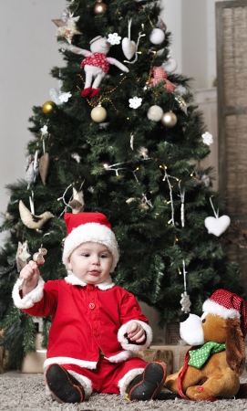 Baby in Santa costume sit near decorating Christmas tree with present toyの写真素材