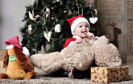 Baby in Santa costume sit near decorating Christmas tree with present toysの写真素材