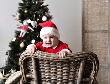 Baby in Santa costume stand on chair near Christmas treeの写真素材