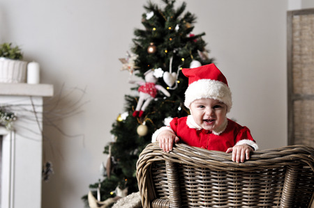 Baby in Santa costume stand on chair near Christmas treeの写真素材
