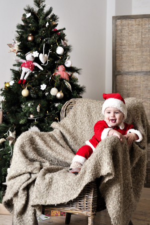 Baby in Santa costume sit on chair near Christmas treeの写真素材