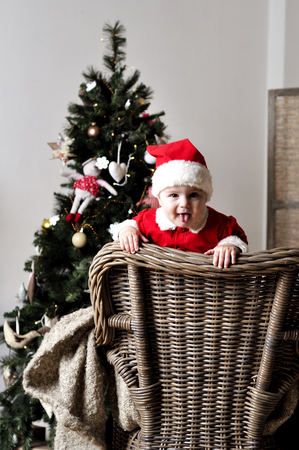 Baby in Santa costume stand on chair near Christmas treeの写真素材