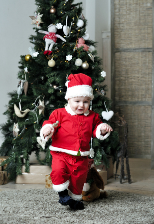 Baby in Santa costume standing on decorating Christmas treeの写真素材