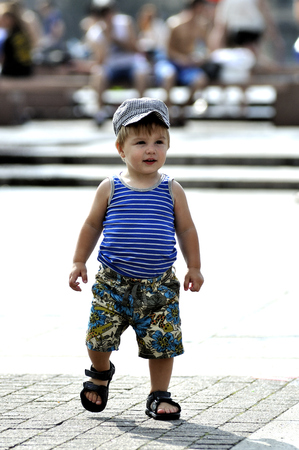 Happy little boy in vest and shorts walks on streetの写真素材