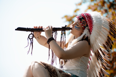 Young woman in war bonnet headdress of American Indian plays on a tree a fluteの写真素材