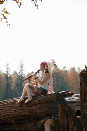 Young woman in war bonnet headdress of American Indian plays on a tree a fluteの写真素材