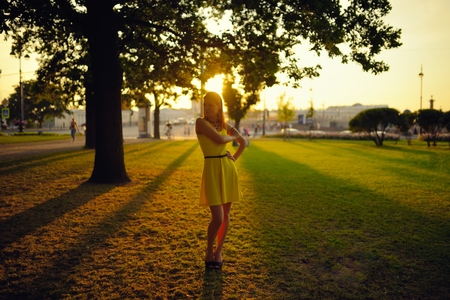 The beautiful girl in a yellow dress stand in beams of the sunset sunの写真素材