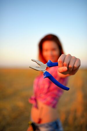 Young woman holds flat nose pliers in a hand at fieldの写真素材