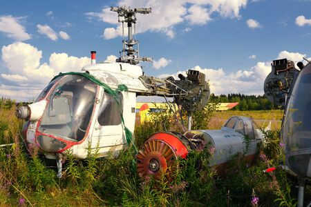 Old airplane fuselage and rusty helicopters on green grassの写真素材