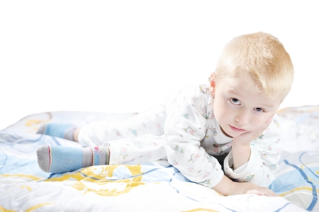 Funny cute little child in pyjamas with blonde hair lies on a bedの写真素材