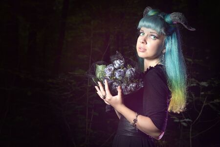 Beautiful woman with color hair and horns in the forest holds a black bouquet
