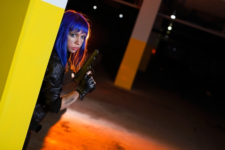 Sexy woman with blue hair holding two guns and looking as killer in underground parkingの写真素材