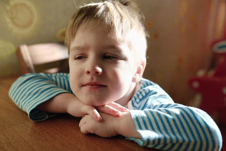 The amusing child sits at a table and cunning looksの写真素材