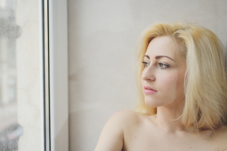 Portrait close up of young beautiful blonde woman near windowの写真素材