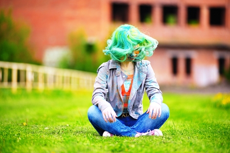Beautiful hipster alternative young woman with green hair sits on grassの写真素材