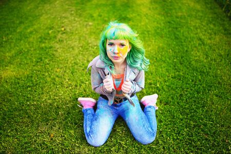 Beautiful hipster alternative young woman with green hair sits on grassの写真素材