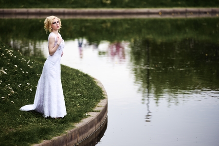 Beautiful young bride in white dress near lake in summer green parkの写真素材