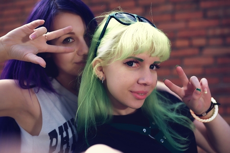 Closeup fashion lifestyle portrait of two young pretty beautiful friends with color hair making selfieの写真素材