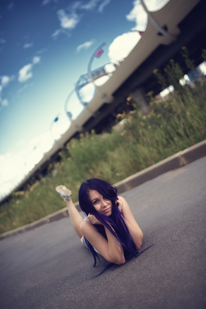 Portrait beautiful young woman with violet hair lying on empty roadの写真素材
