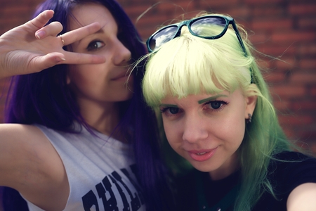 Closeup fashion lifestyle portrait of two young pretty beautiful friends with color hair making selfieの写真素材