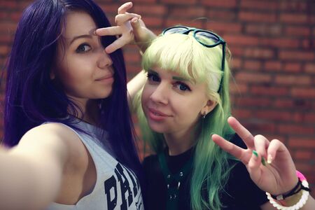 Closeup fashion lifestyle portrait of two young pretty beautiful friends with color hair making selfieの写真素材