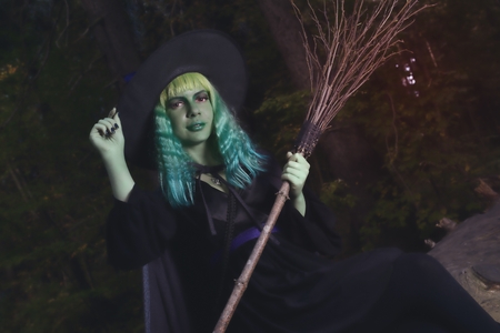 Young girl with green hair and broom in suit of witch in forest. Halloween timeの写真素材