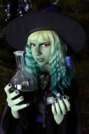 Young girl with green hair and flask with a potion in suit of witch in forest. Halloween timeの写真素材
