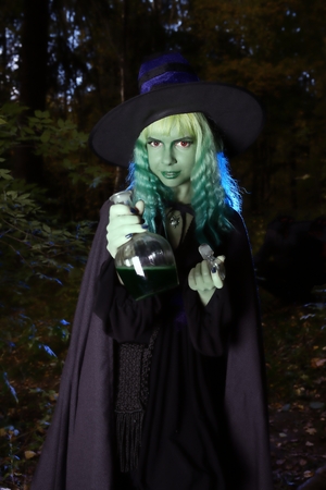 Young girl with green hair and flask with a potion in suit of witch in forest. Halloween timeの写真素材