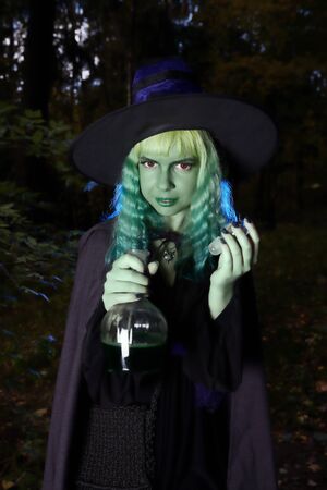Young girl with green hair and flask with a potion in suit of witch in forest. Halloween timeの写真素材