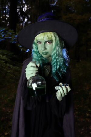 Young girl with green hair and flask with a potion in suit of witch in forest. Halloween timeの写真素材