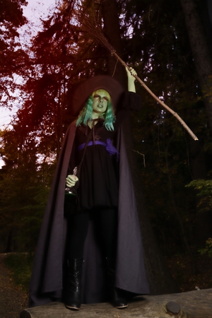 Young girl with green hair and broom in suit of witch in forest. Halloween time