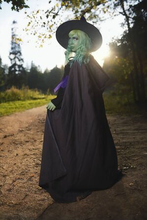 Young girl with green hair and skin suit of witch in forest. Halloween timeの写真素材