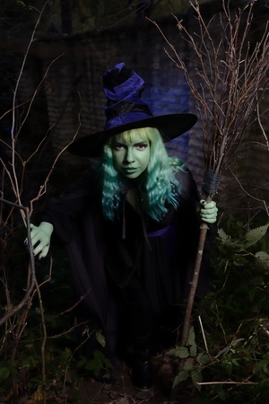Young girl with green hair and broom in suit of witch in forest. Halloween time